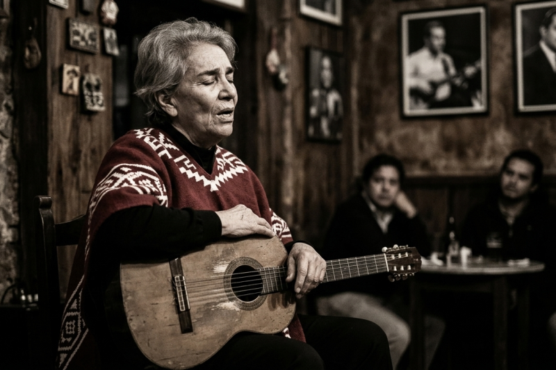 Representación artística de una cantante con poncho tradicional y guitarra en una cantina rústica, evocando la interpretación de Chavela Vargas.